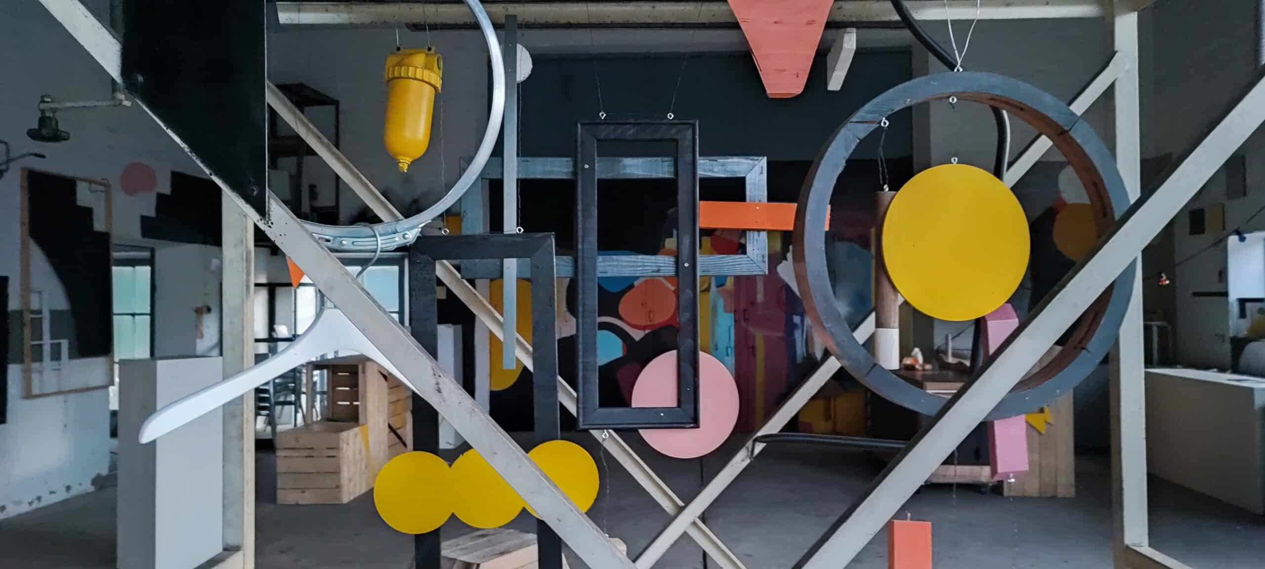 Bunte Formen wie Kreise, Vierecke und Kreuze hängen in einem großen Raum.